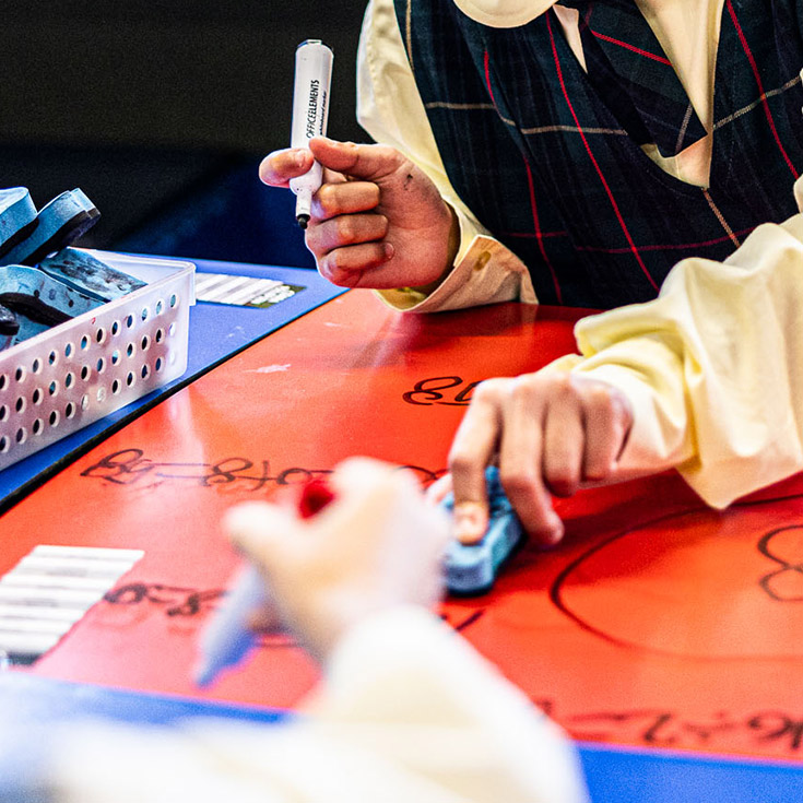 Close up shot of students writing on whiteboard desks at St Aidan's Catholic Primary School Rooty Hill